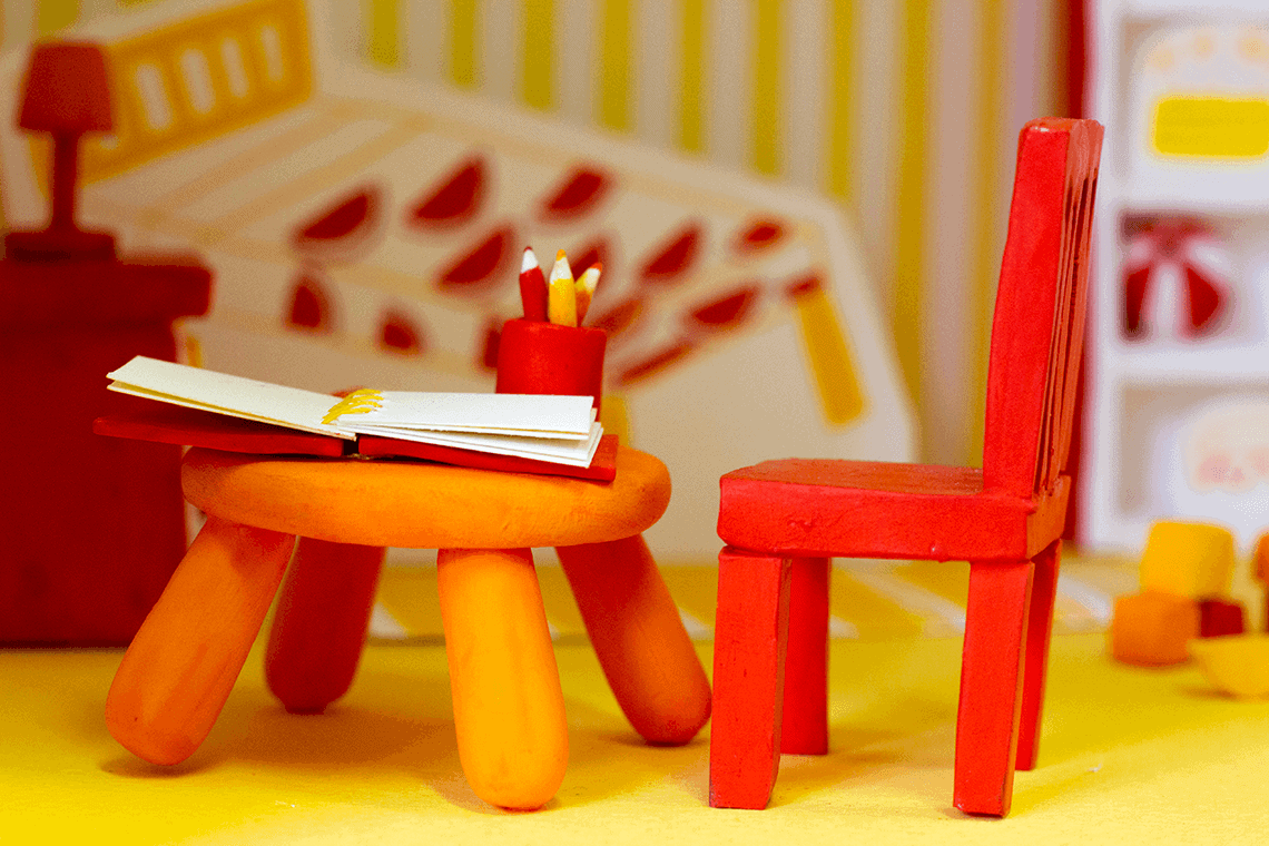 A 3D handmade model of a yellow child's bedroom, made with painted clay and painted paper.
