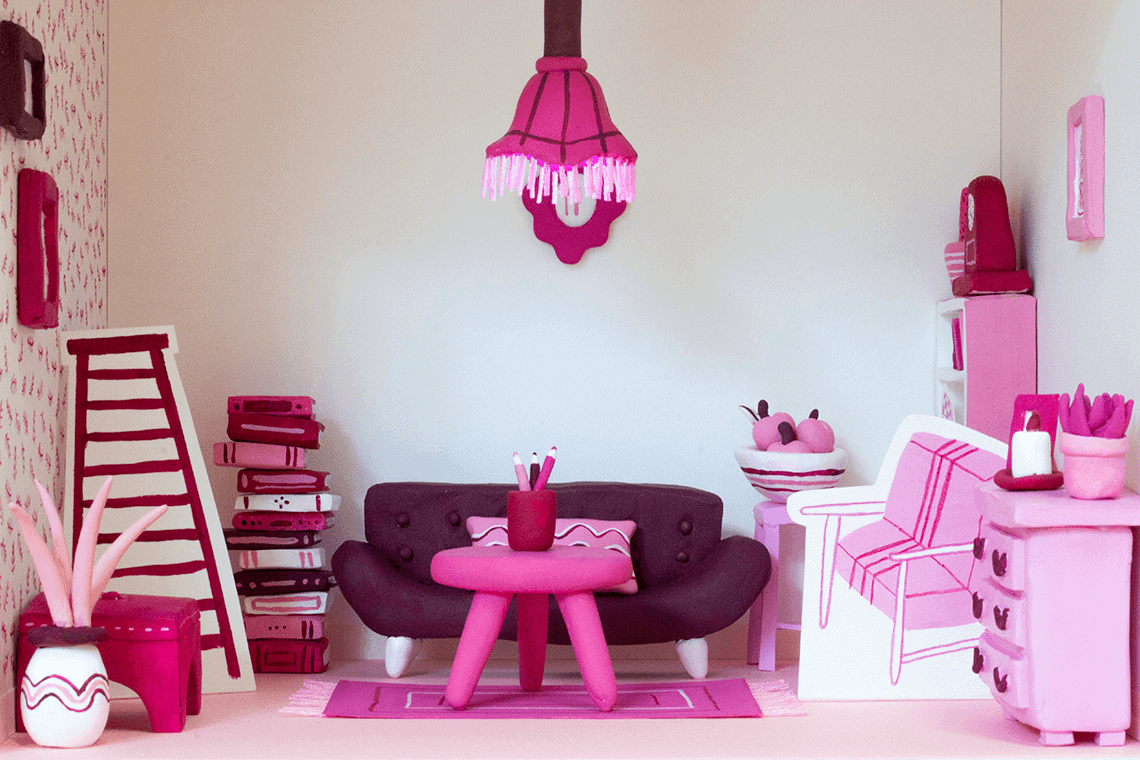 A 3D handmade model of a pink living room made with painted clay and painted paper.